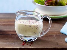 a glass pitcher filled with liquid sitting on top of a wooden table next to a salad