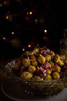 a glass bowl filled with green olives on top of a white plate next to a christmas tree