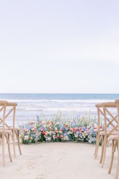 two wooden chairs sitting next to each other on top of a sandy beach near the ocean