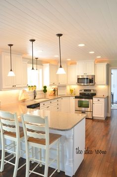 a kitchen with white cabinets and an island in the middle of the room that has four chairs around it