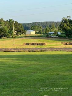 a field with hay bales in the foreground and farm buildings in the background