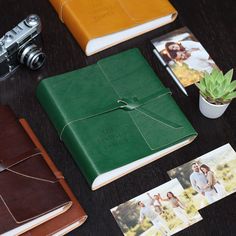 an open green book sitting on top of a table next to two photos and a camera