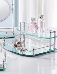 two clear glass vanity trays with perfume bottles on the top and mirror behind them