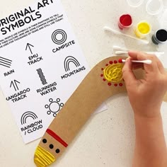 a child's hand is drawing on a cardboard snake with markers and glues