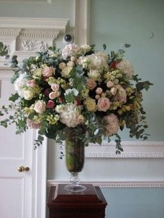 a vase filled with lots of flowers sitting on top of a wooden table next to a mirror