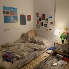 an unmade bed sitting on top of a wooden floor next to a table with a lamp