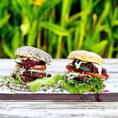 two burgers with lettuce, tomato and other toppings sit on a wooden table