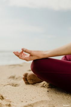 a woman sitting in the sand with her legs crossed and hands folded out to yoga