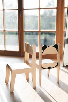 two wooden chairs sitting next to each other on top of a hard wood floor in front of large windows