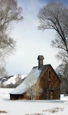 an old barn in the middle of winter with snow on the ground and trees around it