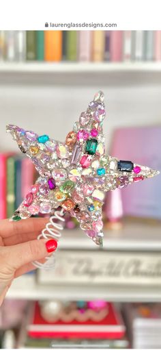 a hand holding a star shaped brooch in front of a book shelf filled with books