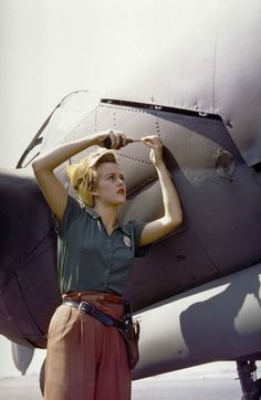 a woman standing in front of an airplane with her hands on the side of it