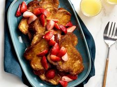 french toast with strawberries and syrup on a blue plate next to a glass of orange juice