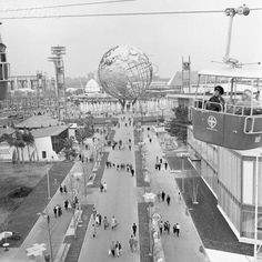 black and white photograph of people walking down the street in front of buildings with giant globe on top