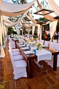 an outdoor dining area with white linens and blue vases on top of the tables