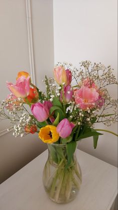 a vase filled with lots of pink and yellow flowers on top of a white table