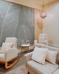 a living room with two chairs and a table in front of a wall decorated with leaves