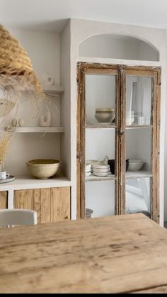 a wooden table sitting in front of a white cupboard filled with plates and bowls on top of it