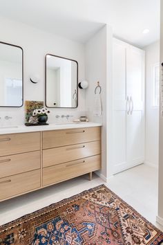 a bathroom with two sinks, mirrors and rug on the floor in front of it