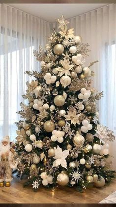 a white christmas tree with gold and silver ornaments on it's top, in front of a window