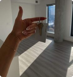 a woman's hand holding a house key in front of a window