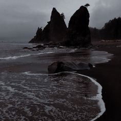 an elephant laying on top of a sandy beach next to the ocean with two large rocks in the background