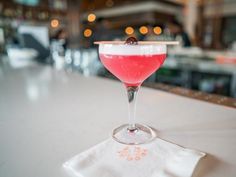 a drink in a wine glass with a cherry garnish on the rim sitting on a napkin