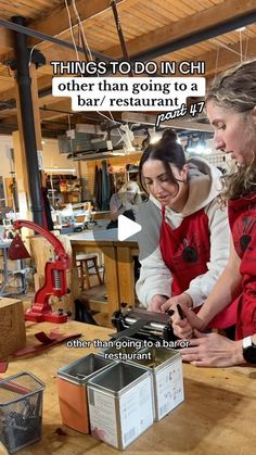 two women in red aprons looking at something on a table