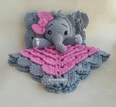 a crocheted elephant sitting on top of a blanket with a pink bow around its neck