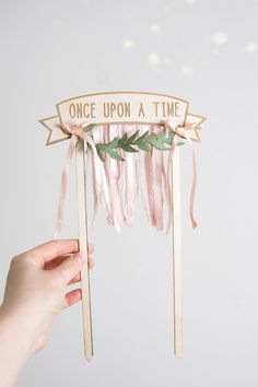 a person holding up a wooden sign that says once upon a time with ribbons around it