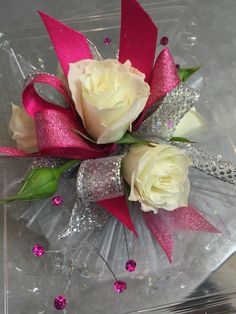 two white roses in a clear vase with pink and silver decorations on the bottom side