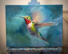 a painting of a hummingbird in flight on a easel with paintbrushes