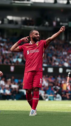 a man in red uniform standing on top of a soccer field with his arms outstretched