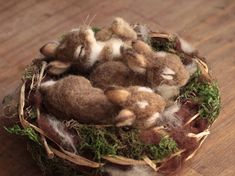 several small stuffed animals in a nest on a wooden surface with grass and twigs around them