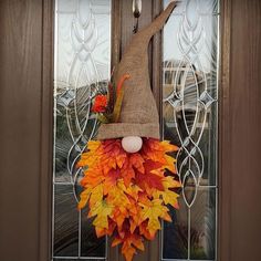 a scarecrow door hanger decorated with fall leaves and an egg in the center