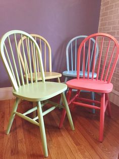 three wooden chairs sitting next to each other on top of a hard wood floor in front of a purple wall