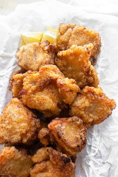 some fried food sitting on top of a piece of wax paper with lemon wedges