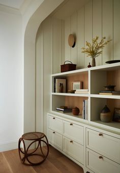 a white book shelf with books and vases on it's shelves next to a wooden floor