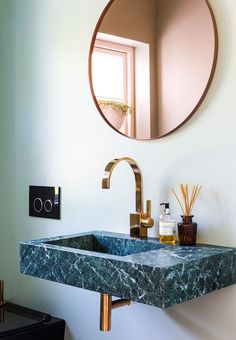 a bathroom sink sitting under a round mirror next to a wall mounted faucet