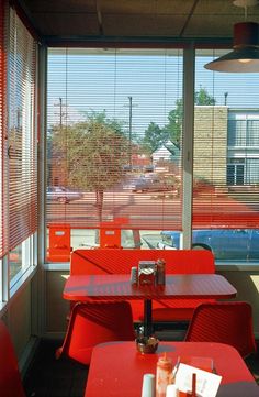 red tables and chairs in front of a window with blinds on the windowsills