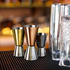 three metallic cups sitting on top of a table next to a glass filled with water