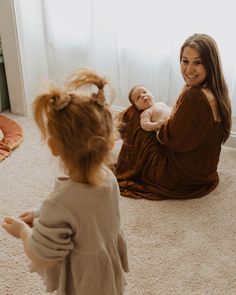 a woman sitting on the floor with a baby in her lap and another person standing next to her