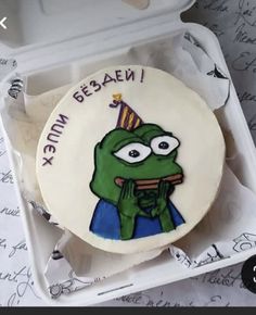 a decorated cookie in a white box with writing on the side and an image of a green frog wearing a party hat