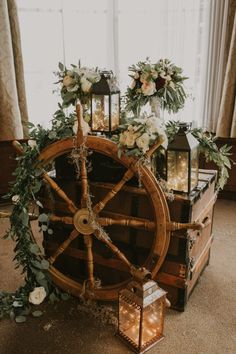 a wooden wheel decorated with flowers and greenery on the floor next to two lanterns