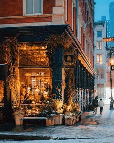 people walking down the street in front of a flower shop on a snowy day at night