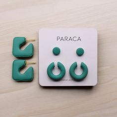 two pairs of green earrings sitting on top of a wooden table next to each other