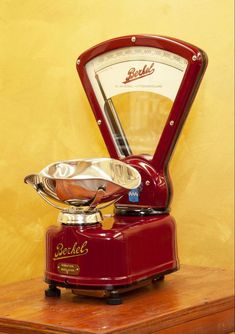 an old fashioned coffee grinder sitting on top of a wooden table next to a yellow wall