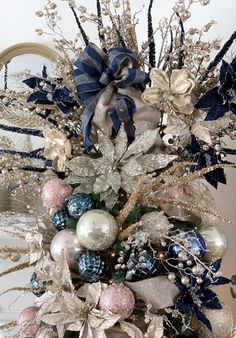 a christmas tree decorated with blue, silver and white ornaments in a vase next to a mirror