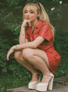 a woman in a red dress is sitting on a wooden platform with her hand under her chin