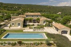 an aerial view of a house with a swimming pool in the foreground and trees surrounding it